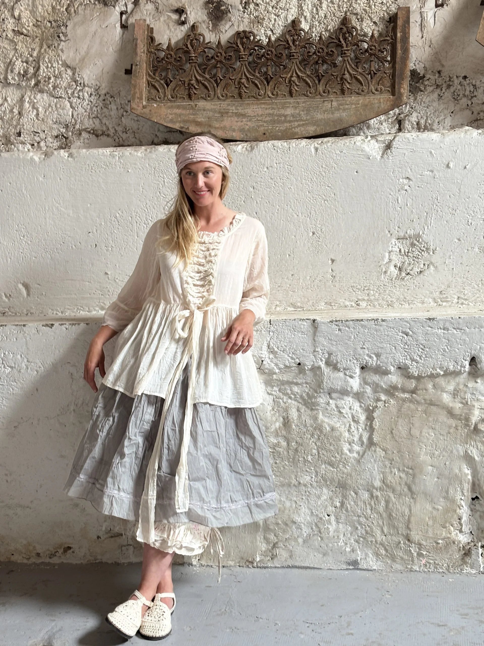 Female model leaning against textured concrete wall in Les Ours clothing including bandana, skirt and jacket