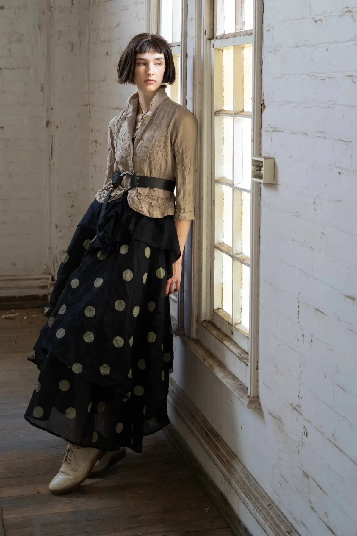 Woman in Dogstar  a long black polka dot skirt standing in a room with white walls and wooden floor.