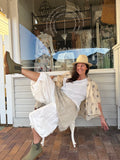 Woman sitting on a chair in front of a store window with a white dress and straw hat.