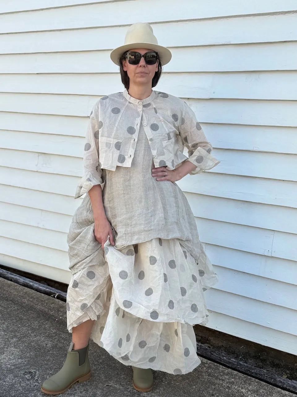 Person wearing a layered outfit with polka dot and plain pieces, standing against a white wall.