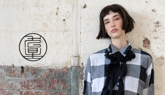 Person wearing a dogstar checkered shirt and black scarf against a textured wall with a brand logo.