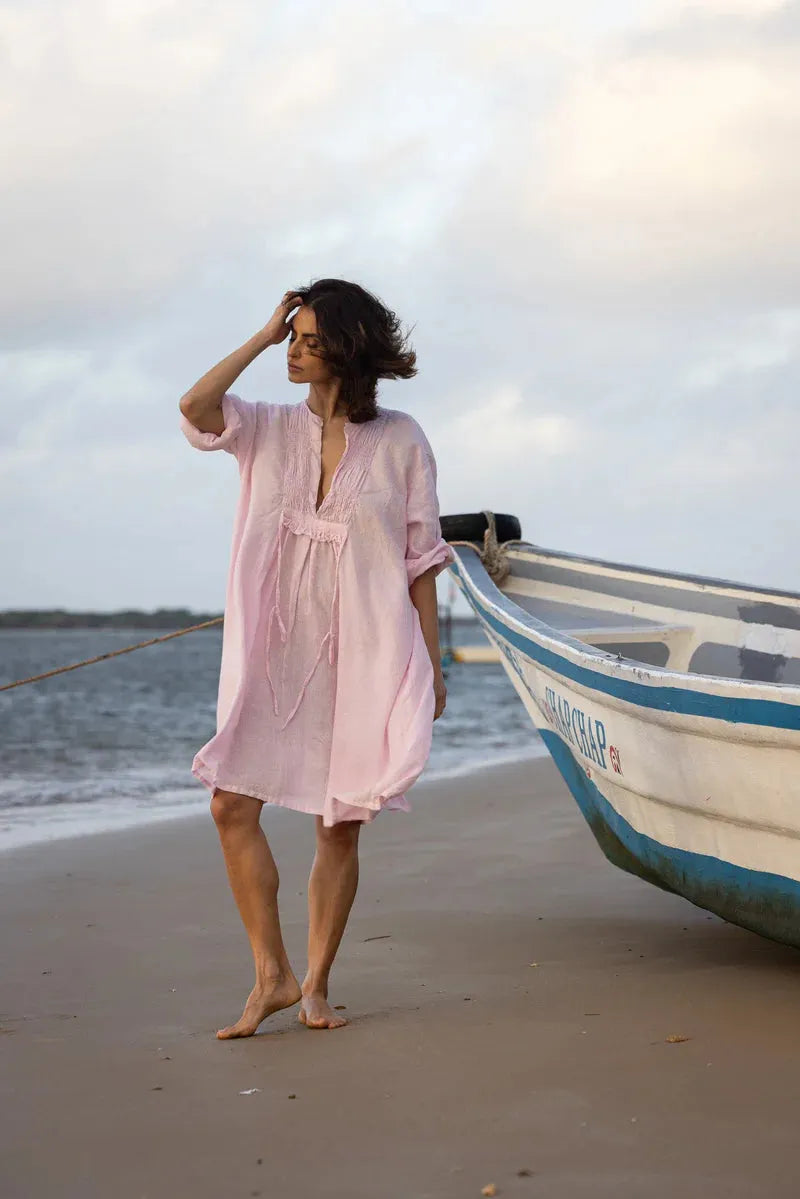 Woman in a Meg by Design pink dress standing on a beach with a boat in the background