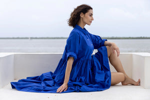 Woman in a blue Meg by Design Dress sitting on a white bench with a blurred background